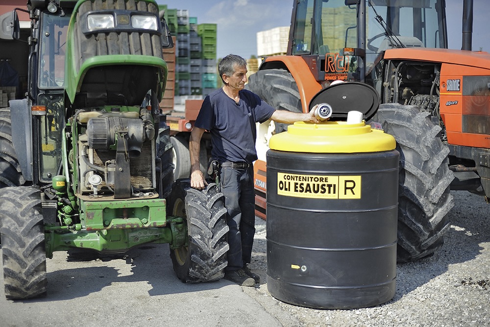 Technician opening a waste oil collection tank between two farm tractors
