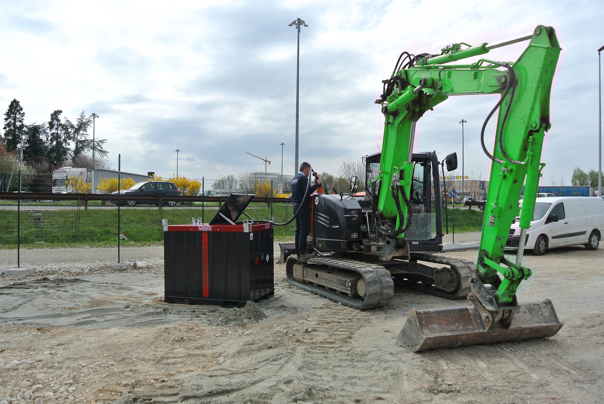 Man refueling a green excavator from a containerized fuel tank on a job site