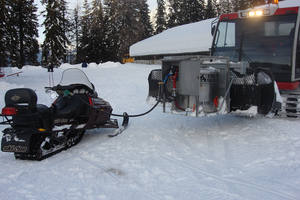 Snowcat refueling a snowmobile with a front-mounted fuel enclosure in a snowy forest