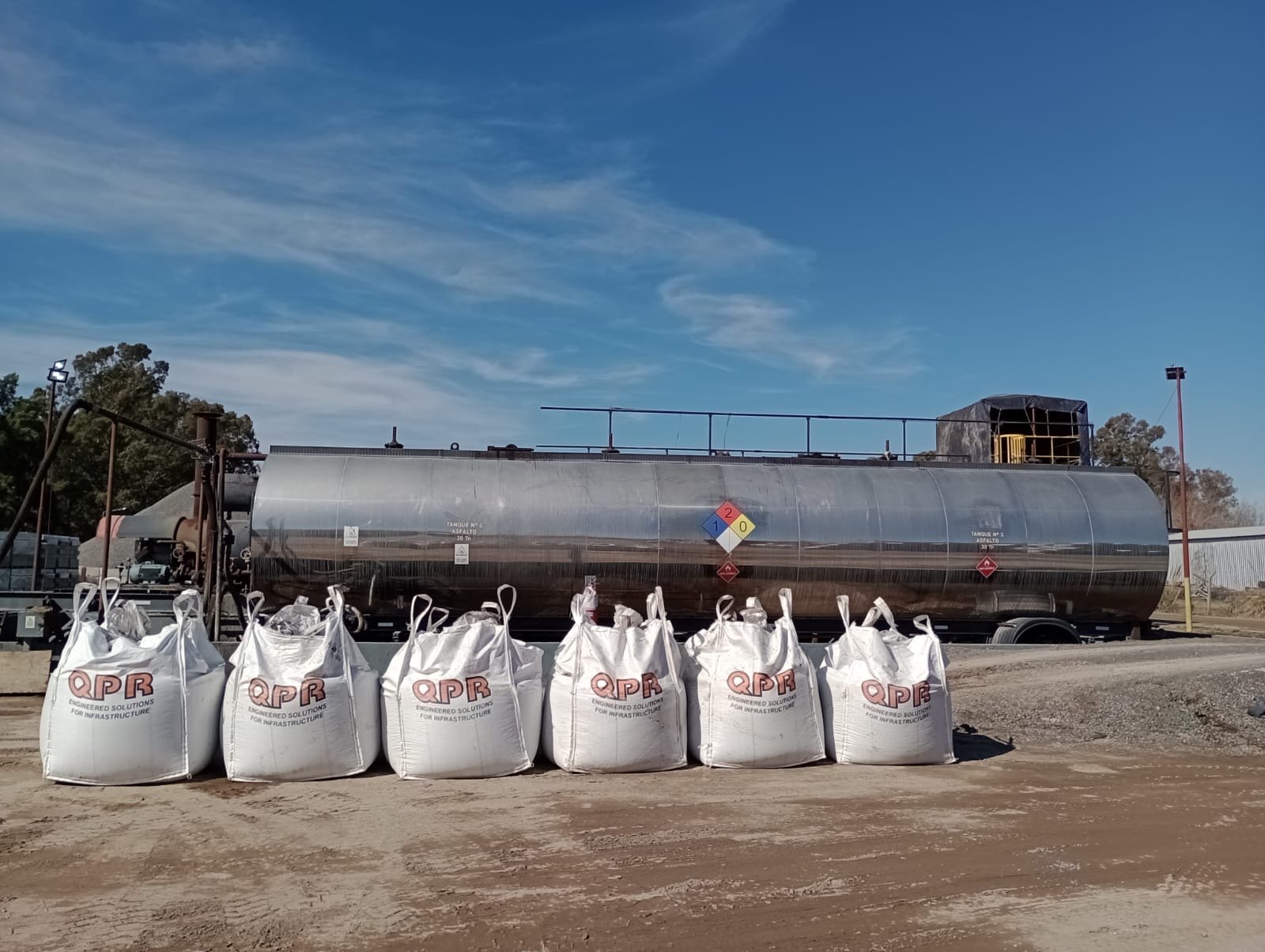 Row of QPR bulk bags of cold mix asphalt in front of an asphalt tanker at a production plant