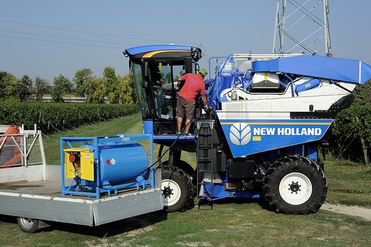 Blue transportable fuel tank on a flatbed refueling a vineyard harvester in the field